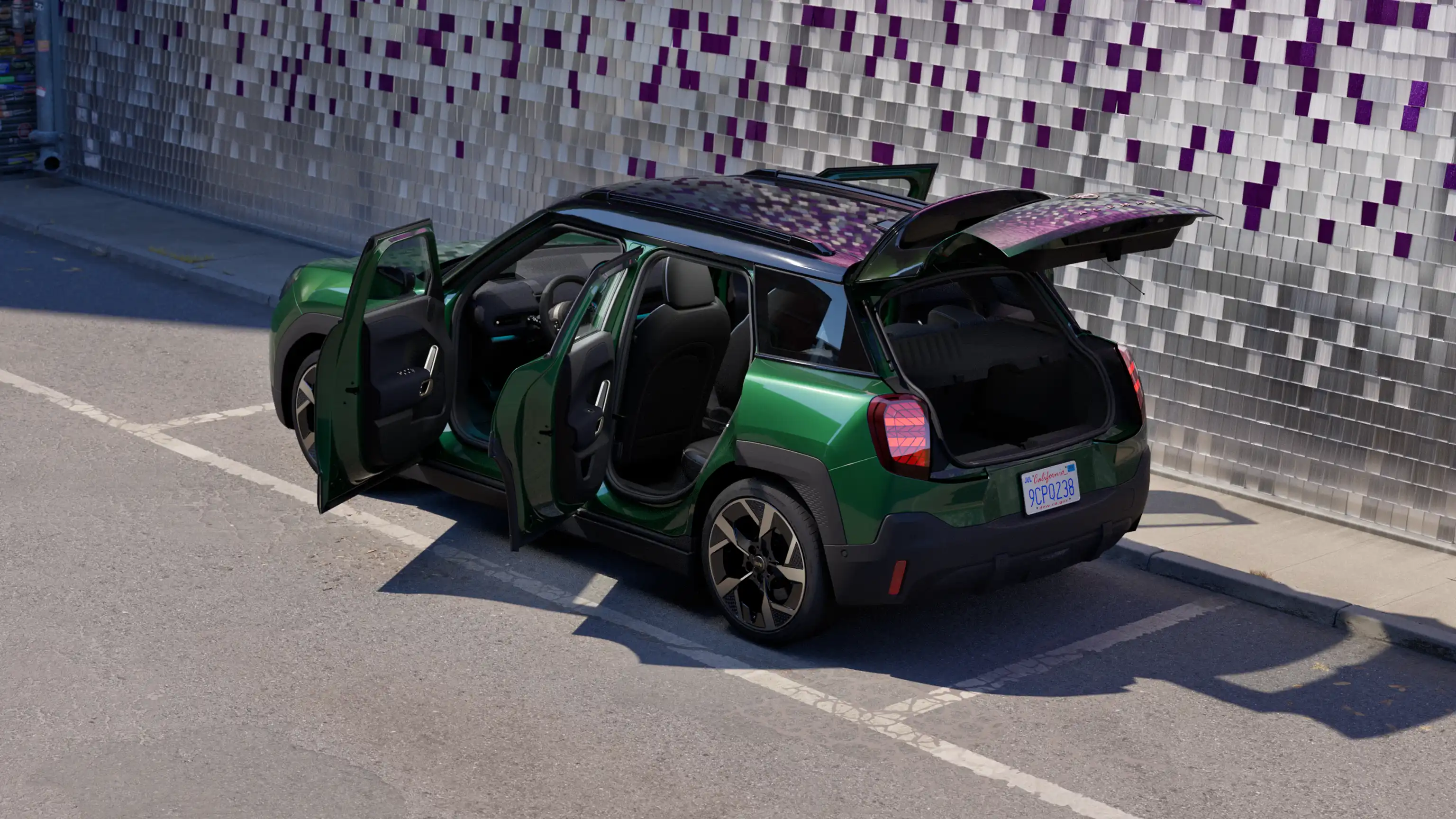 Seitliche Heckansicht eines vollelektrischen MINI Aceman in British Racing Green mit geöffneten Türen, der auf einem Parkplatz parkiert, mit einer farbigen Wand im Hintergrund