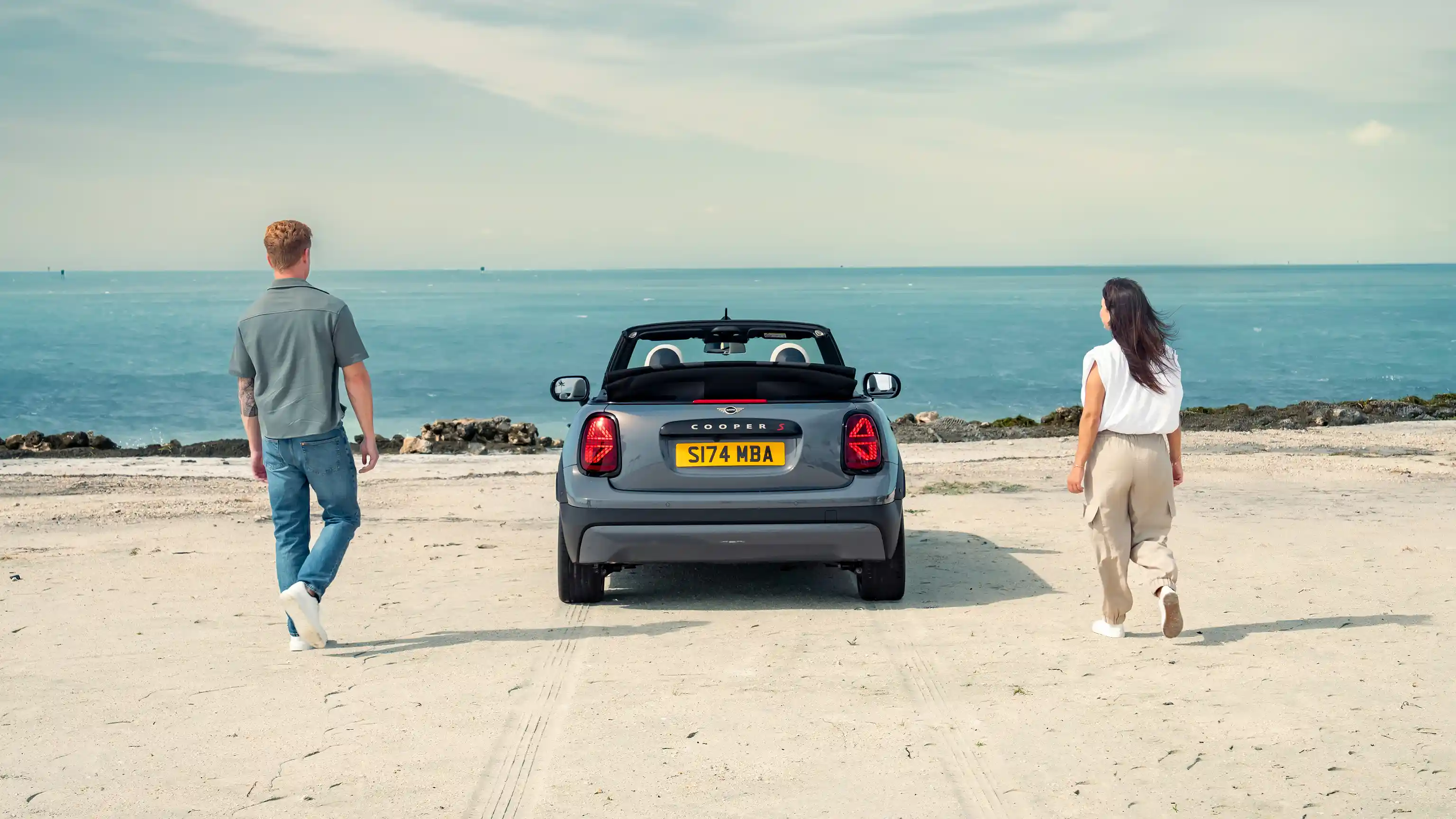 Heckansicht eines parkenden MINI Cooper Cabrio an einem Strand mit zwei Personen