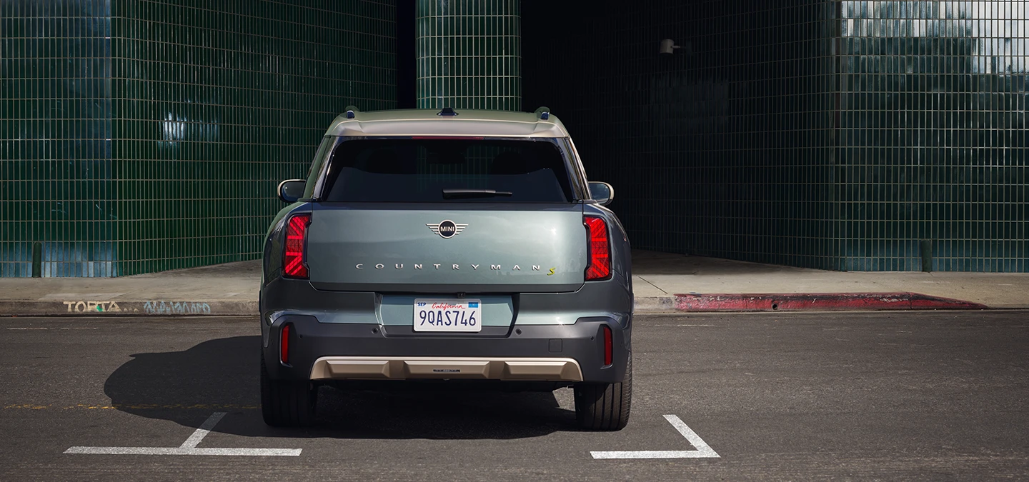 Heckansicht eines parkenden vollelektrischen MINI Countryman in Smokey Green mit Dach in Vibrant Silver. 