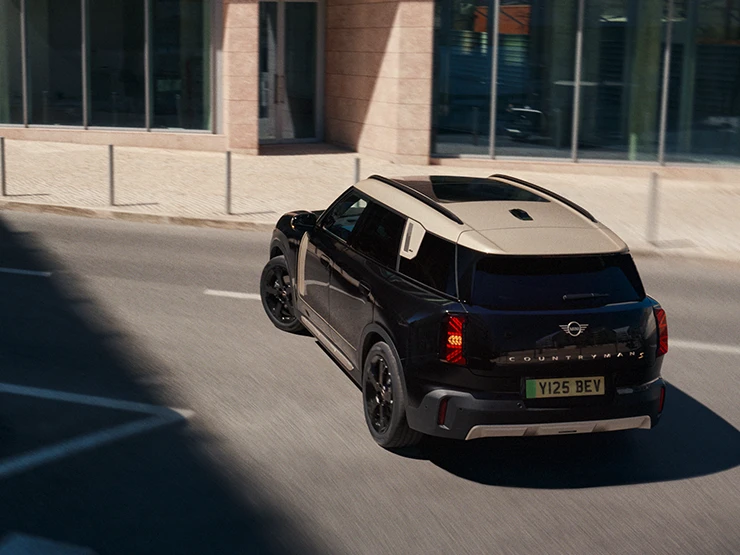 Ansicht von hinten oben eines parkenden vollelektrischen MINI Countryman in Midnight Black mit Dach in Vibrant Silver.