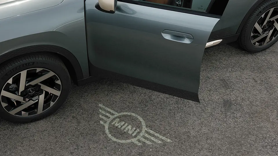 Außenansicht des MINI Countryman mit geöffneter Tür und Begrüßungslicht mit MINI Logo auf dem Boden