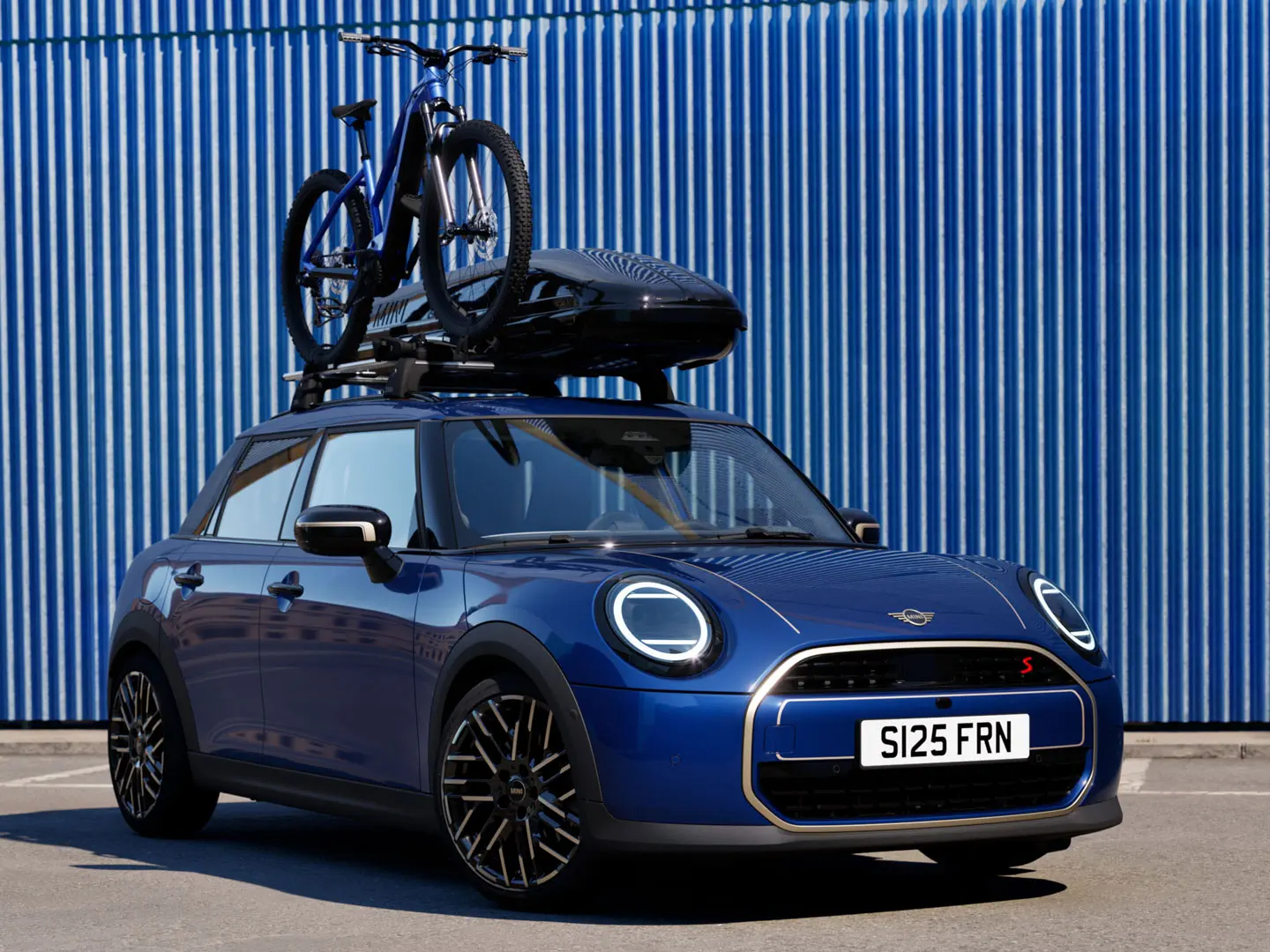 Vorderansicht des MINI Aceman in Indigo Sunset Blue mit MINI Fahrraddachträger mit Mountainbike und MINI Dachbox 320.
