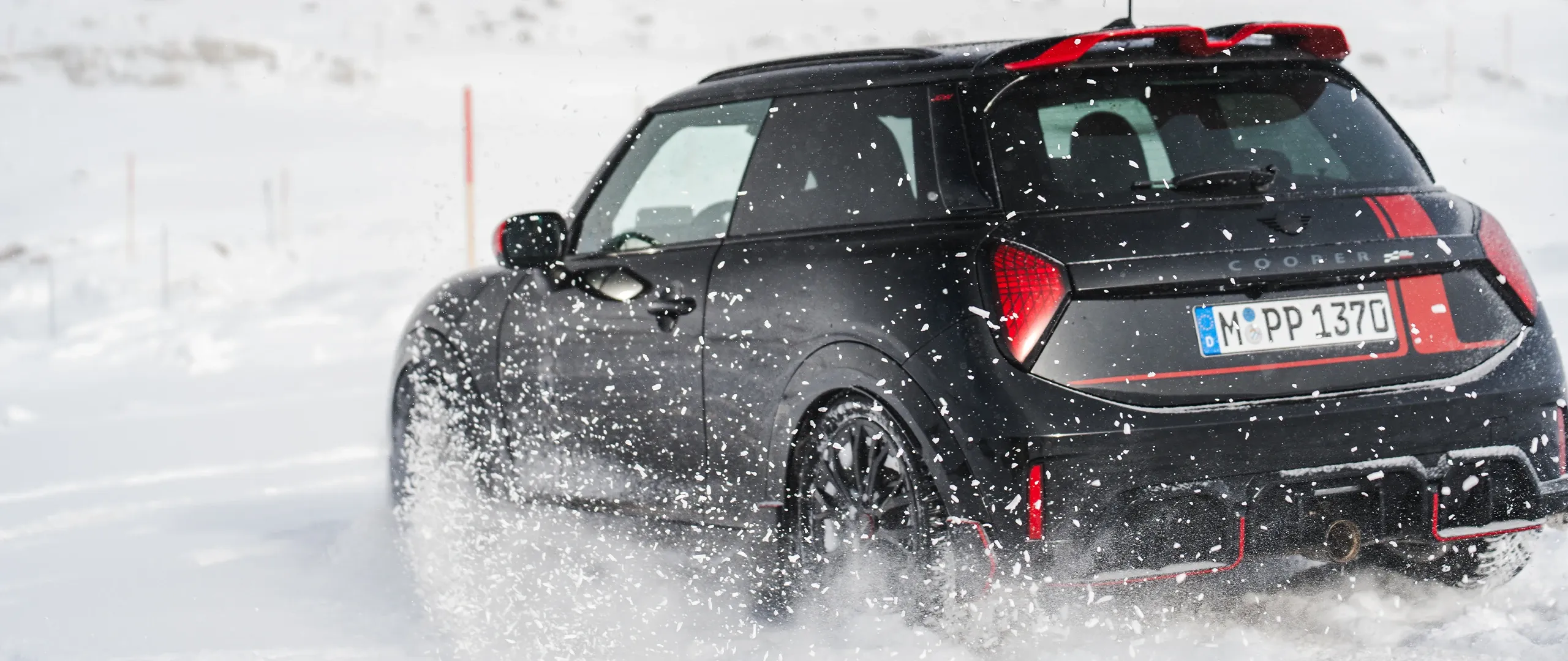 Ansicht von hinten auf einen MINI Cooper JCW, der durch den Schnee fährt.