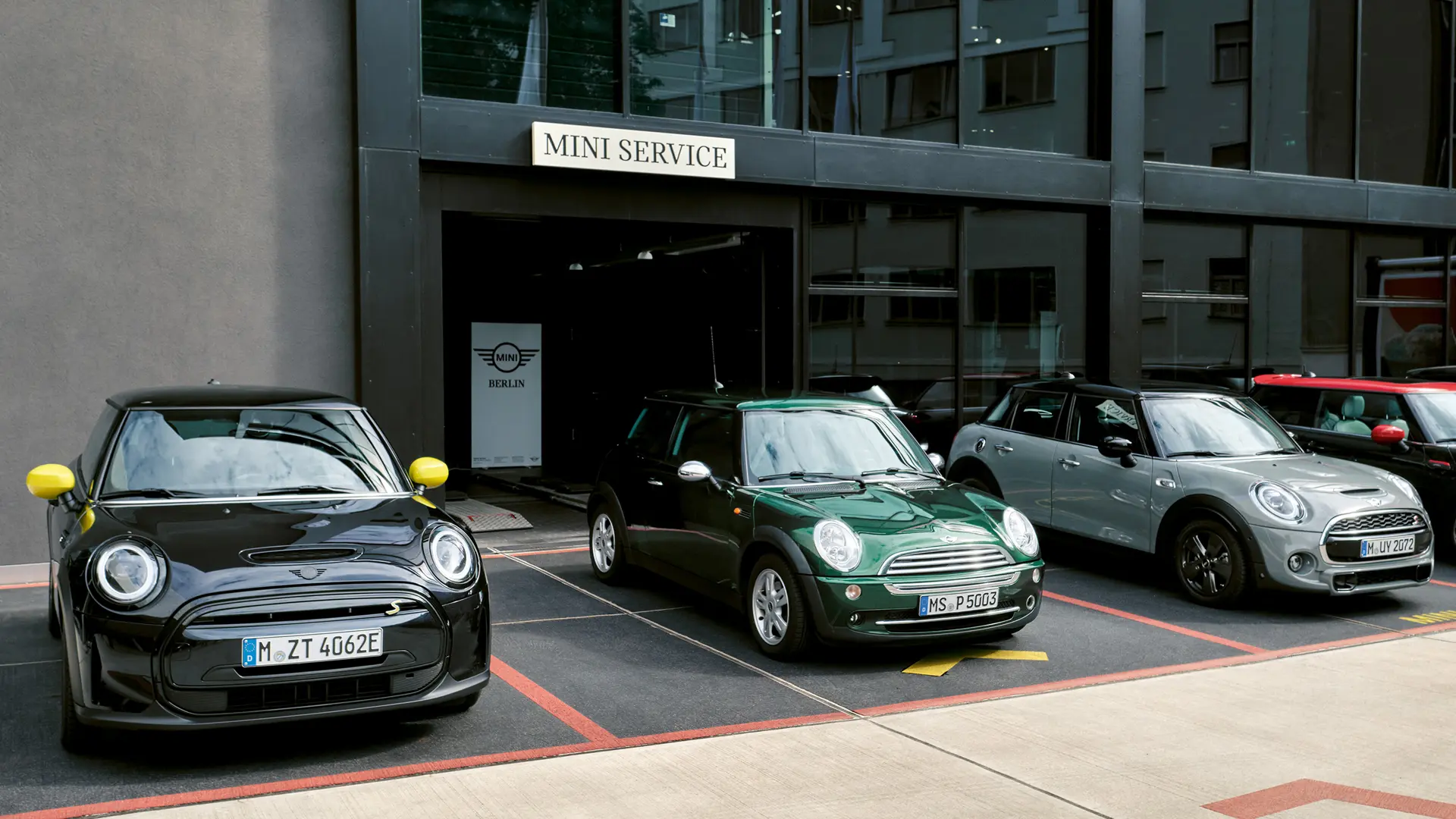 MINI Cooper Electric S in schwarz steht vor einem MINI Partner neben einem MINI Cooper 3-Türer in grün, MINI 5-Türer in silber, MINI JCW schwarz, Frontansicht. 