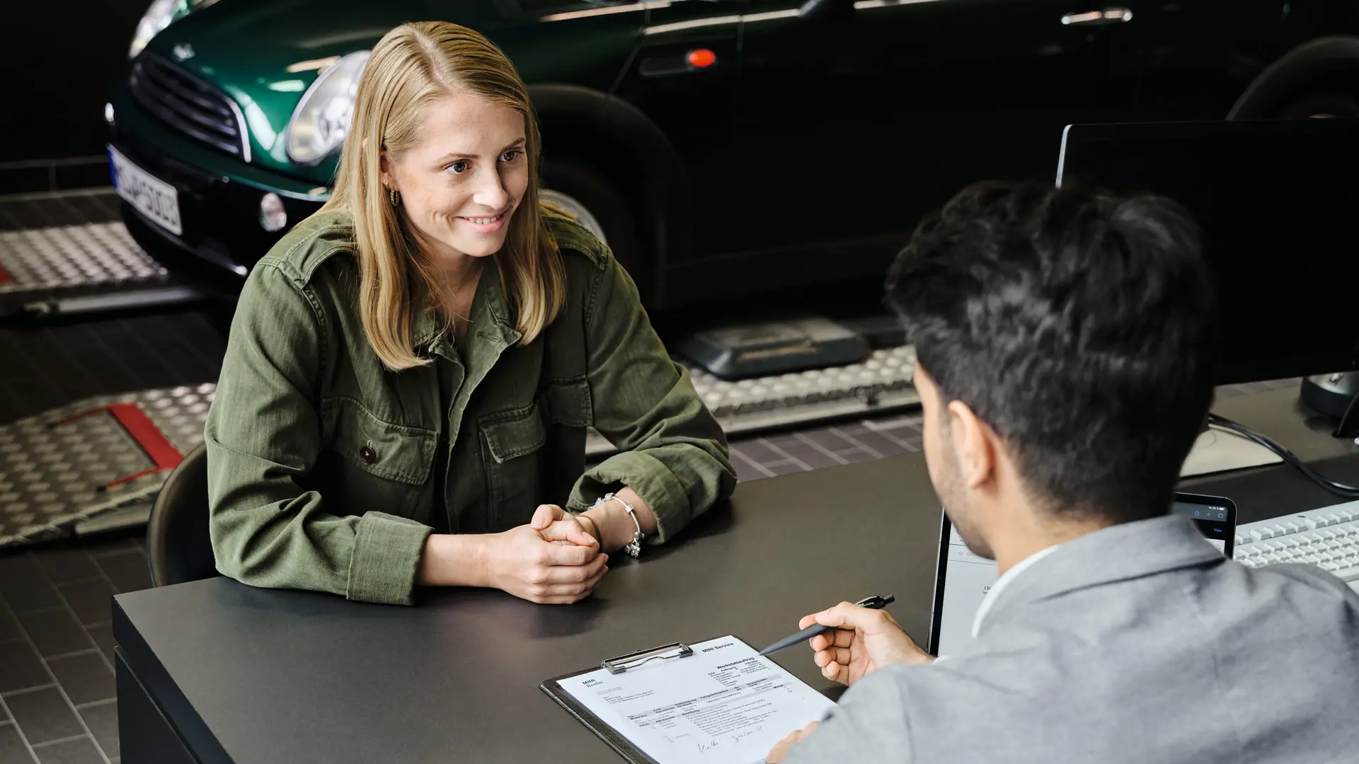 MINI Partner mit Berater, der die Kundin über ihre Serviceoptionen berät, beide sitzen an einem Tisch.