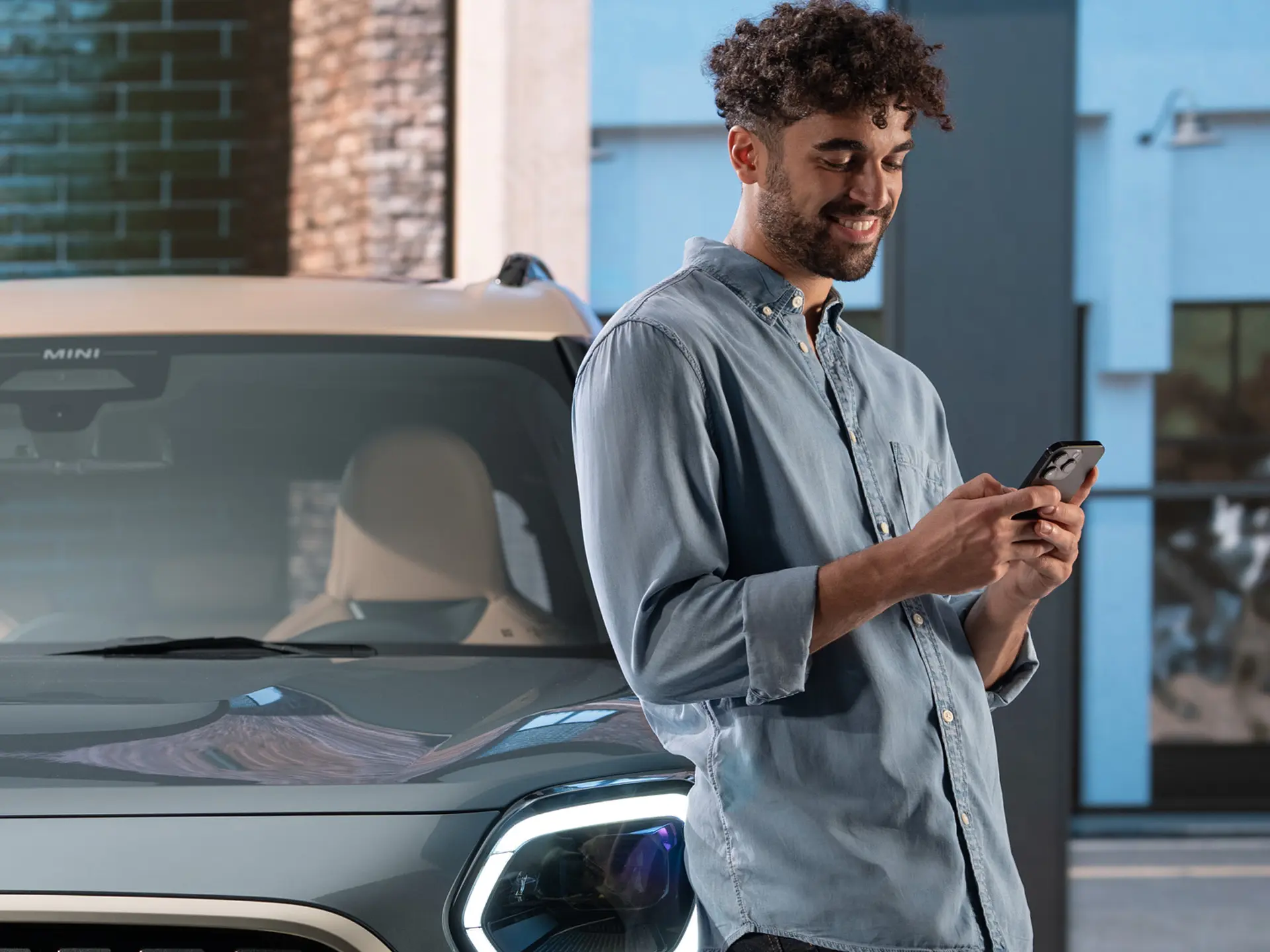 Personalisierte MINI Servicetermine - ein Mann tippt auf seinem Handy neben einem MINI