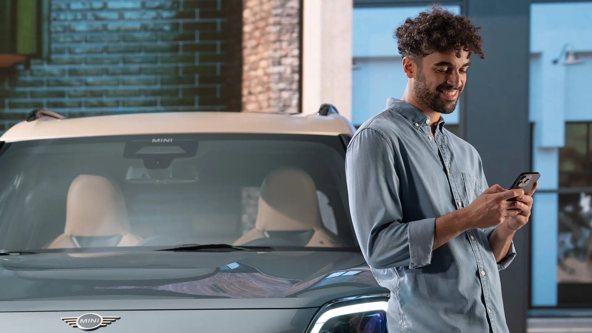 Personalisierte MINI Servicetermine - ein Mann tippt auf seinem Handy neben einem MINI