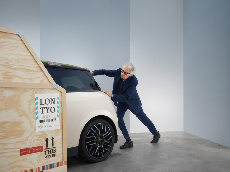 Rückansicht des vollelektrischen MINI Cooper Paul Smith Edition in Inspired White mit Paul Smith hinter dem Auto.