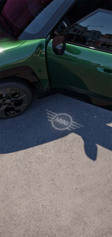 Aussenansicht des vollelektrischen MINI Aceman mit geöffneter Tür und Begrüssungslicht mit MINI Logo auf dem Boden