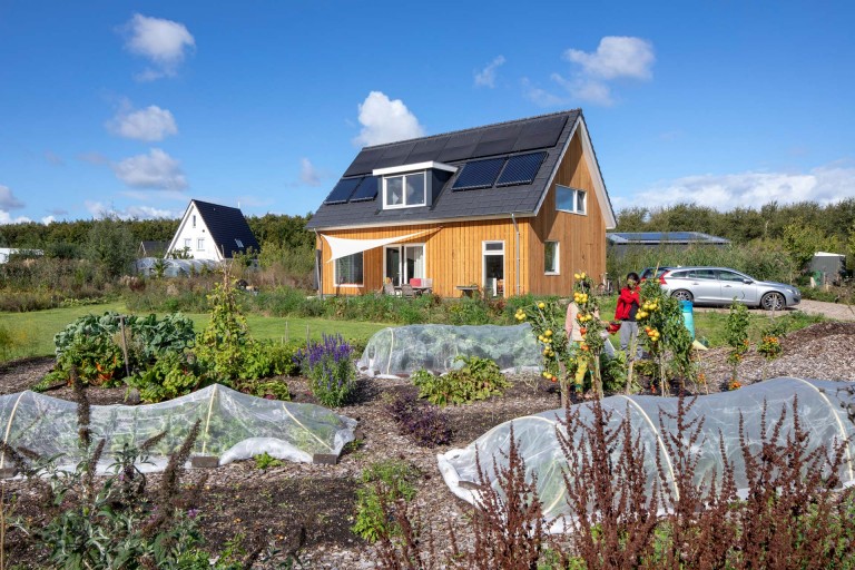 Mo0v eines Holzhauses mit Garten. Auf dem Dach des Hauses wurden Solarmodule angebracht.