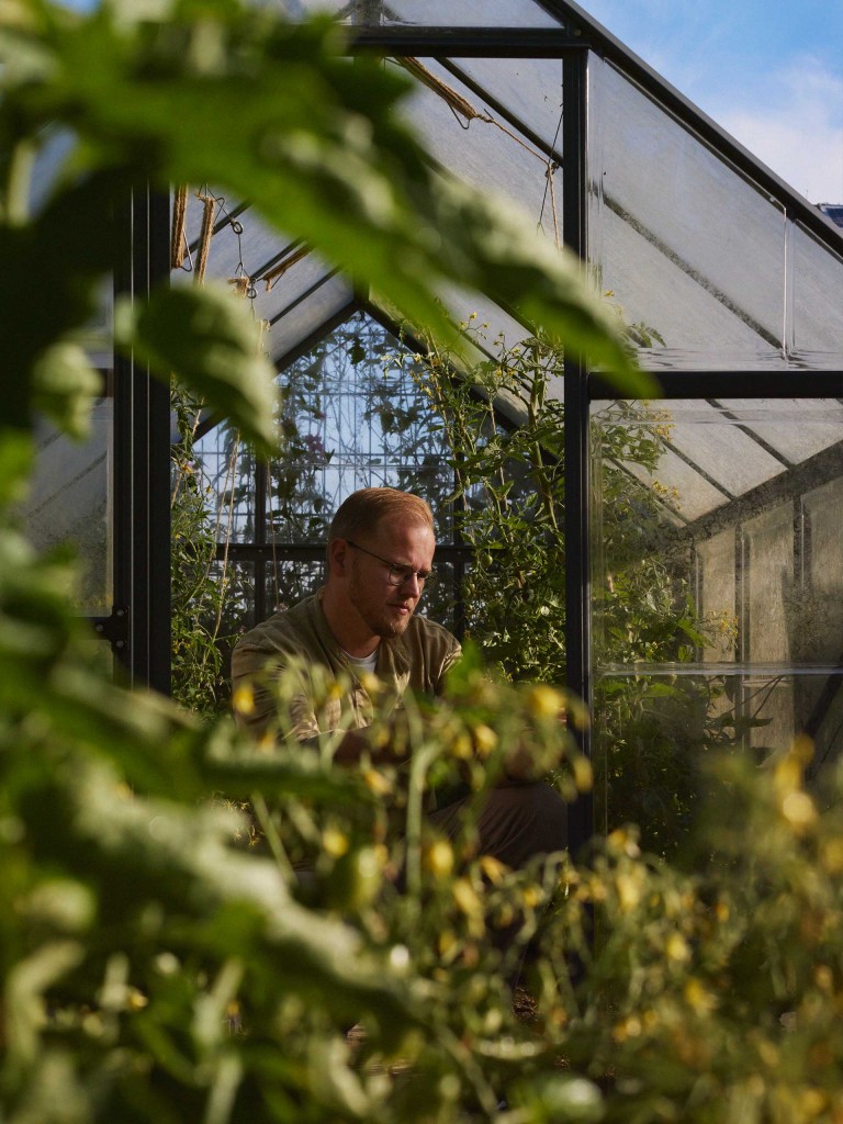 Jens kniet in seinem Gewächshaus vor seinem selbst angebauten Gemüse der Saison.
